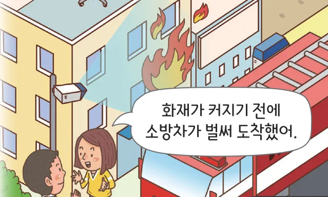 불이 난 건물 앞에 소방차가 와 있고 사람들이 이야기하는 장면